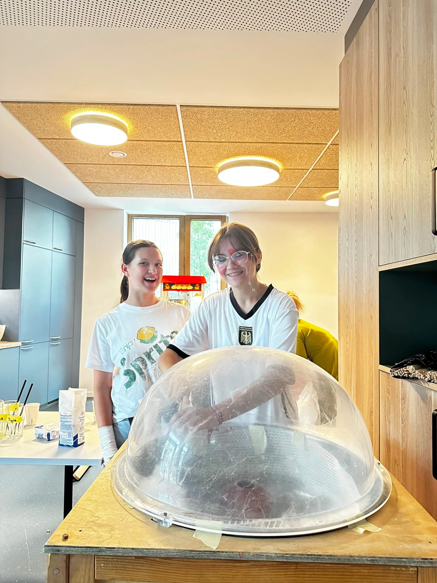 Zwei junge Frauen hinter einer Zuckerwattemaschine im Nachbarschaftszentrum, lachend und im Gespräch mit den Gästen des Mondschein-Events.