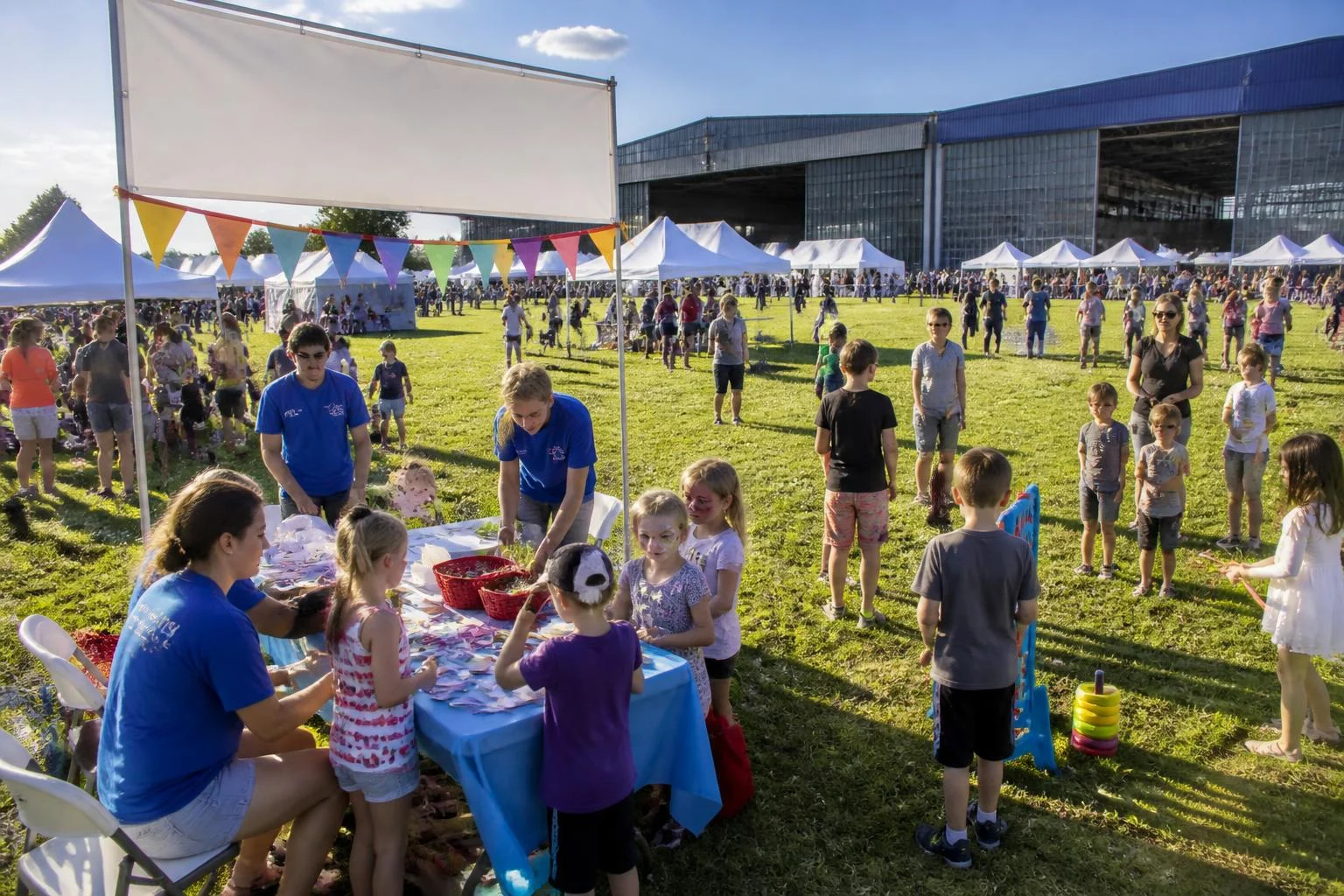 Familienfest auf grüner Wiese mit vielen Pavillons und Ständen, im Vordergrund ein Mitmach-Stand mit vielen Kindern